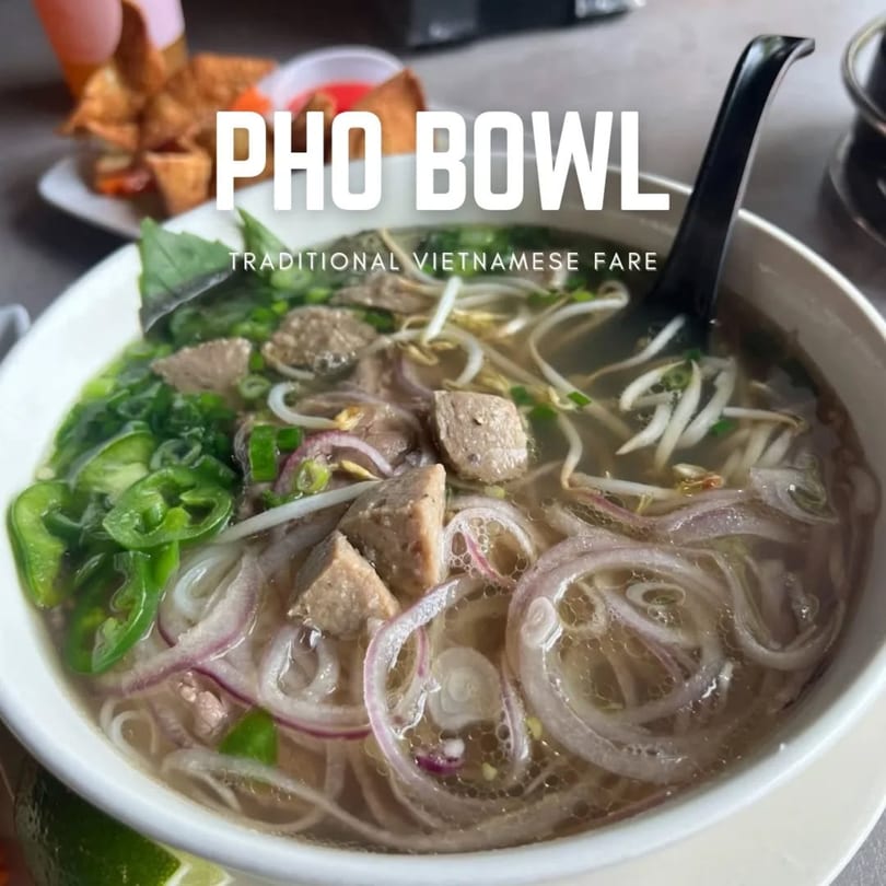 A close-up of a Pho Bowl with noodles, meat, onions, and green herbs, with a black spoon.