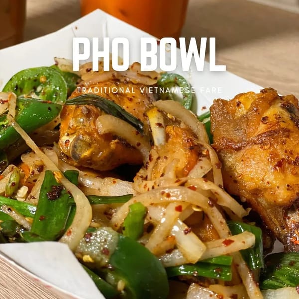 Close-up of Pho Bowl's fried chicken wings with onions and green peppers in a white container.