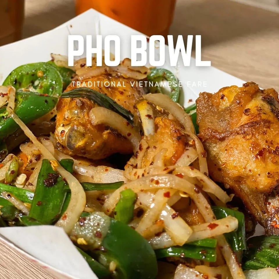 Close-up of Pho Bowl's fried chicken wings with onions and green peppers in a white container.
