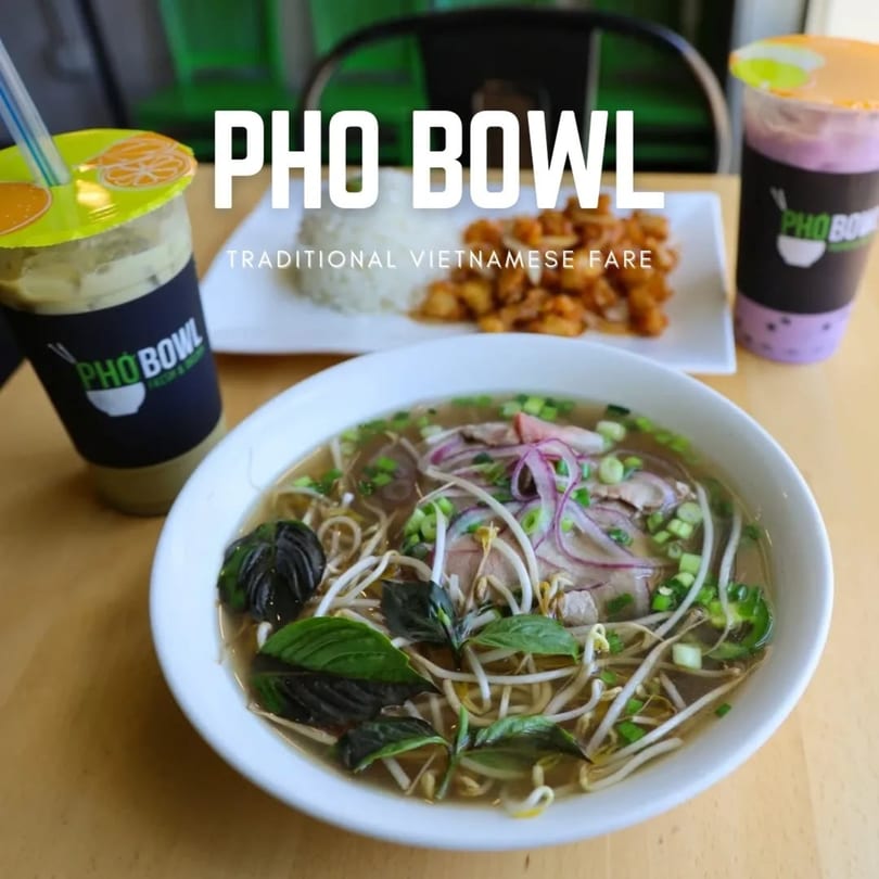 A bowl of Pho with basil, bean sprouts, and onions, alongside rice, chicken, and two drinks.