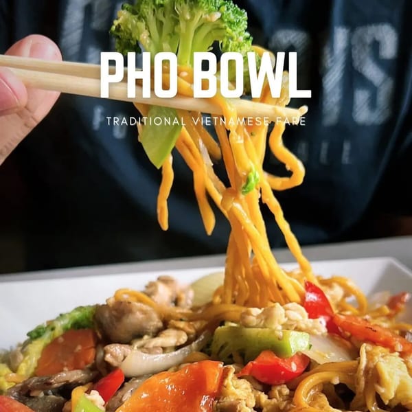 Chopsticks lifting noodles and broccoli from a bowl of Pho Bowl's traditional Vietnamese fare.